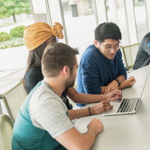 Three students gathered around a MacBook.