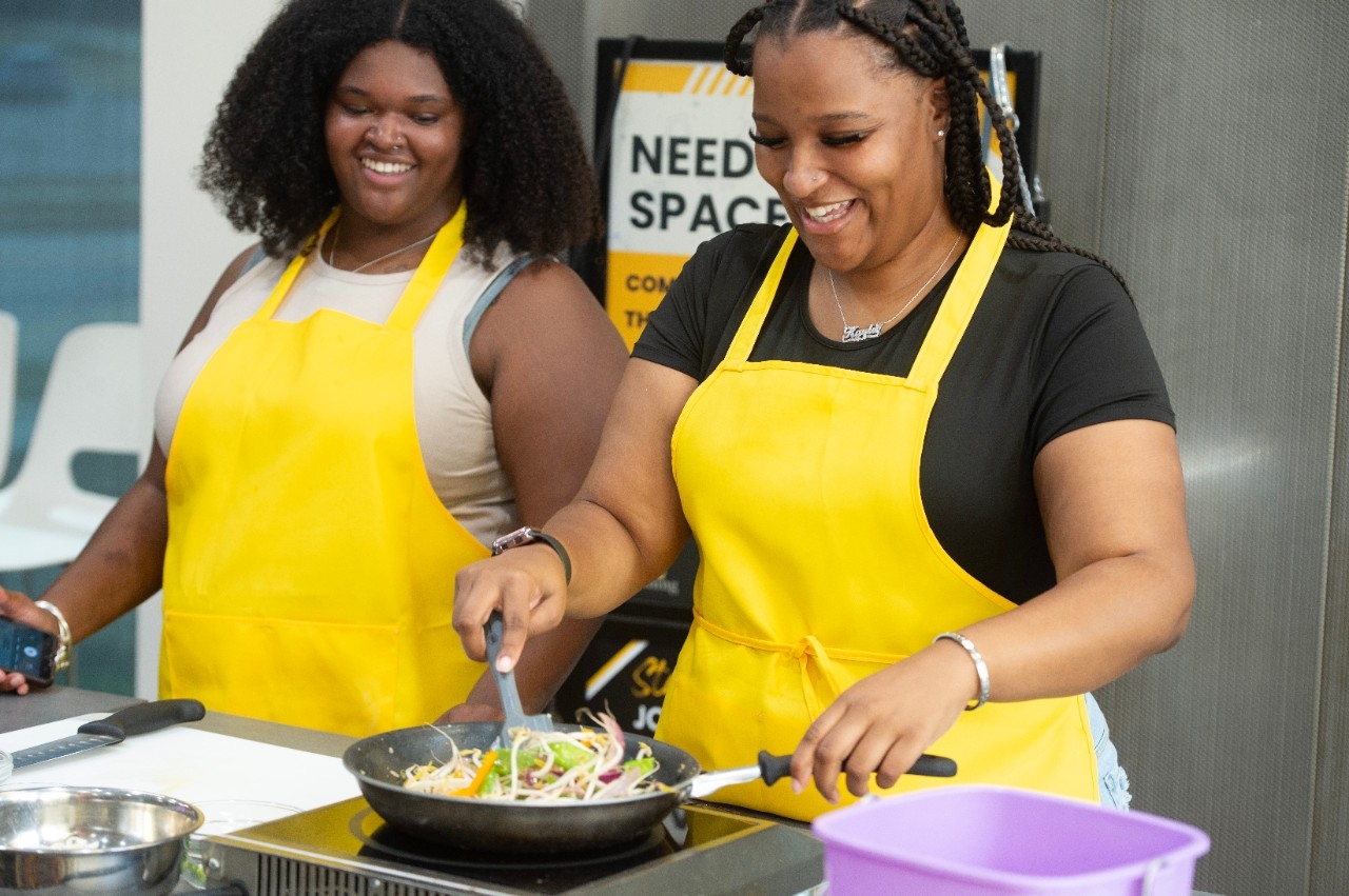 Two women smile as they cook during a wokrshop at a Family Day event 