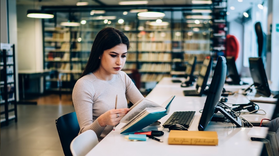 A woman studies with a book and a computer