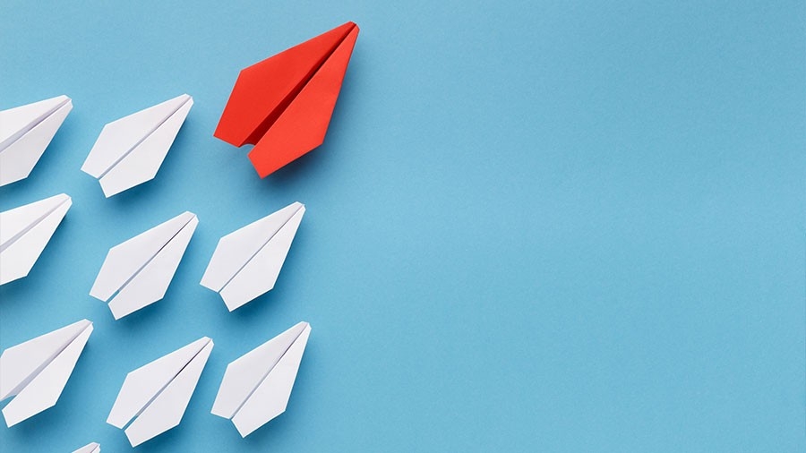 red paper airplane leading a group of white paper airplanes